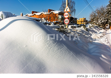 Pristine white snow mounds heap along the sunlit highway shoulder, with urban rooftops peeking under a vibrant winter sky 141556320