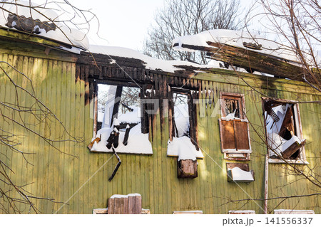 Abandoned wooden house, charred by fire, stands starkly in winter. Snow covers the burnt ruins, revealing a scene of profound devastation 141556337