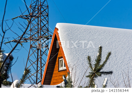 Charming winter dacha roof blanketed in pristine snow against a crisp blue sky. Cozy cabin retreat with a triangular gable and bright window, nestled in frosty nature Charming winter dacha roof blanketed in pristine snow against a crisp blue sky. Cozy cabin retreat with a triangular gable and bright window, nestled in frosty nature 141556344