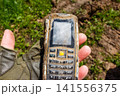 A push-button mobile phone that has been in the ground for a long time lies on the palm 141556375