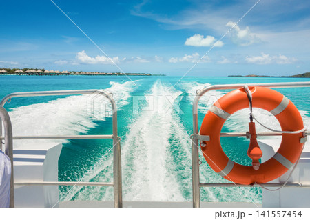 Boat wake across crystal clear tropical lagoon near luxury overwater resort villas Boat wake across crystal clear tropical lagoon near luxury overwater resort villas 141557454