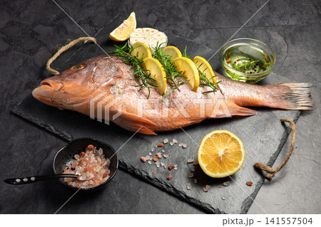 Freshly marinated raw Red snapper fish with lemon slices, garlic and rosemary herbs, on dark background 141557504