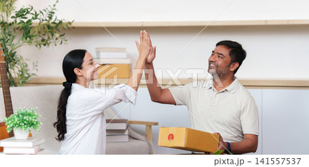 Happy diverse couple high fiving after receiving e-commerce delivery package at home Happy diverse couple high fiving after receiving e-commerce delivery package at home 141557537