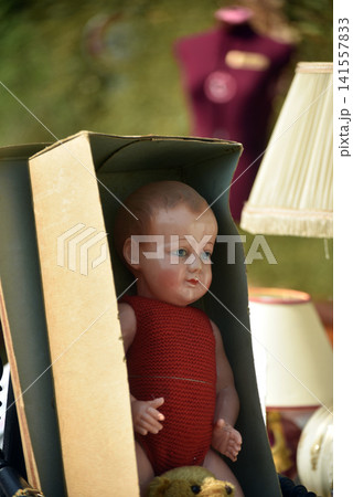 Beautiful vintage porcelain baby doll displayed among old objects at a flea market, showing a nostalgic atmosphere with antique treasures and childhood memories. 141557833