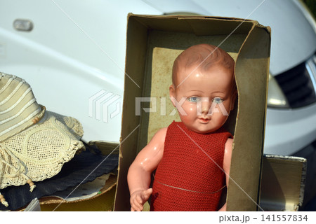 Beautiful vintage porcelain baby doll displayed among old objects at a flea market, showing a nostalgic atmosphere with antique treasures and childhood memories. 141557834