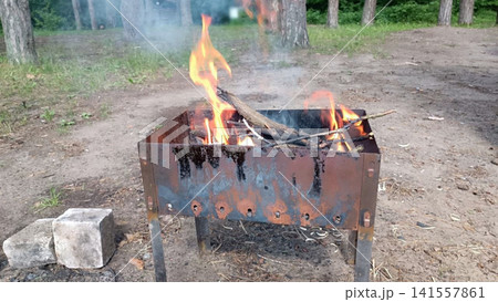 Rusty metal fire pit burning wood in forest clearing with smoke and orange flames Rusty metal fire pit burning wood in forest clearing with smoke and orange flames 141557861