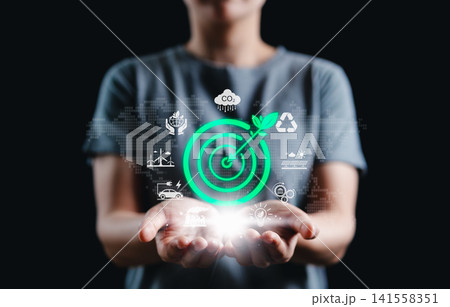 Renewable energy and Sustainability Concept. Woman holds green target icon with leaf arrow, surrounded by eco-friendly and sustainability symbols, environmental responsibility, and sustainable goals. Renewable energy and Sustainability Concept. Woman holds green target icon with leaf arrow, surrounded by eco-friendly and sustainability symbols, environmental responsibility, and sustainable goals. 141558351