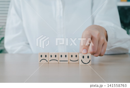 Customer Review and Satisfaction Feedback Concept. Choosing smiling face emoji from row of wooden cubes with different expressions, customer satisfaction, service rating, and experience feedback. Customer Review and Satisfaction Feedback Concept. Choosing smiling face emoji from row of wooden cubes with different expressions, customer satisfaction, service rating, and experience feedback. 141558763