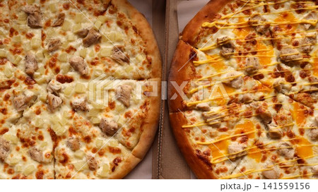 Two delicious round pizzas in boxes. On the left is a chicken fillet, juicy pineapple, and mozzarella. On the right is a chicken fillet with melted cheddar and zigzags of yellow sauce. Two delicious round pizzas in boxes. On the left is a chicken fillet, juicy pineapple, and mozzarella. On the right is a chicken fillet with melted cheddar and zigzags of yellow sauce. 141559156