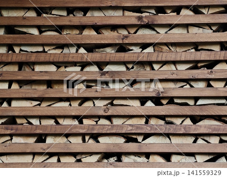 Stacked split firewood behind horizontal wooden slats 141559329
