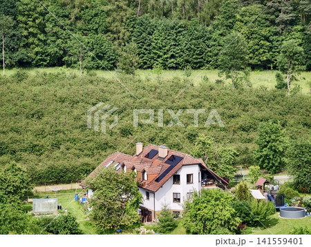 House with solar panels surrounded by green hillside and garden House with solar panels surrounded by green hillside and garden 141559401