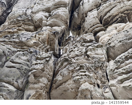 Weathered limestone cliff face with deep fissures and textured erosion 141559544
