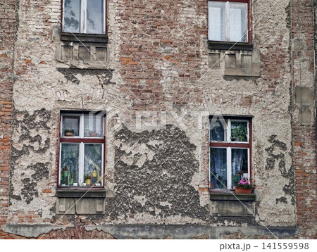 Weathered brick apartment facade with peeling plaster and four windows 141559598