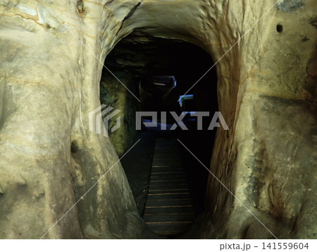 Narrow passageway through limestone cave with wooden walkway into darkness 141559604