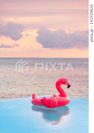 Trendy pink flamingo float on calm ocean at golden sunset tropical beach soft pastel sky. Perfect summer vacation travel lifestyle paradise. Fun luxury getaway leisure scenic 141559620