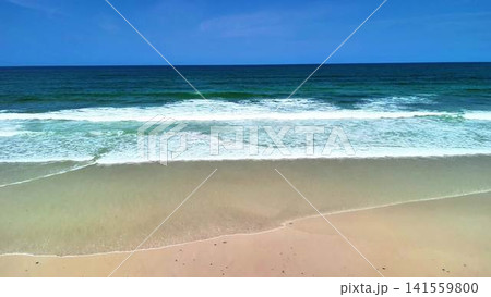 Experience the Beauty of Ocean Waves Gently Meeting the Shoreline Under a Clear Blue Sky 141559800