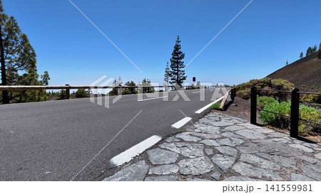 A scenic mountain road beautifully adorned with lush greenery and clear blue skies above A scenic mountain road beautifully adorned with lush greenery and clear blue skies above 141559981