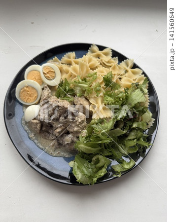 Plate of pasta, salad, and sliced boiled eggs on a black dish Plate of pasta, salad, and sliced boiled eggs on a black dish 141560649
