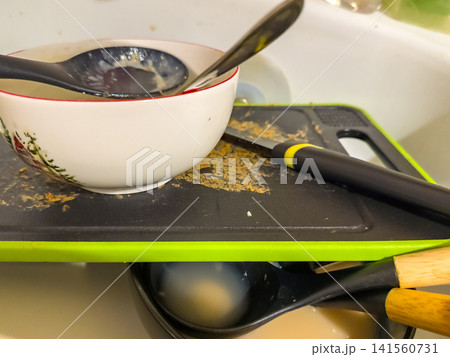 Dirty dishes and utensils stacked on cutting board in kitchen sink Dirty dishes and utensils stacked on cutting board in kitchen sink 141560731