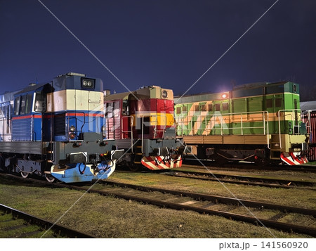 Locomotives rest in shadows. Various engines arranged along tracks with shadows cast in quiet yard Locomotives rest in shadows. Various engines arranged along tracks with shadows cast in quiet yard 141560920