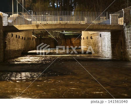 Gloomy riverside scene. Quiet city underpass illuminated by amber reflections and shadowed archways 141561040