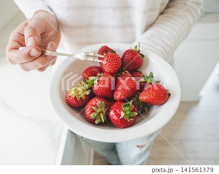 Woman's hands hold a white bowl with strawberries 141561379