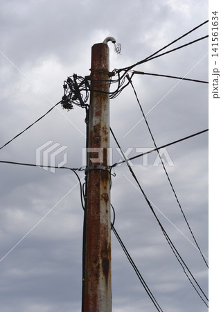 Old Rusty Utility Pole with Power Lines Against Cloudy Sky 141561634