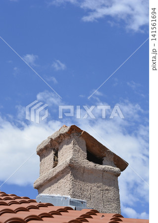 Traditional stone chimney on a roof against a blue sky with clouds. Traditional stone chimney on a roof against a blue sky with clouds. 141561694