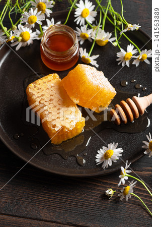 Golden honeycomb on black plate with chamomile flowers, fresh honey Golden honeycomb on black plate with chamomile flowers, fresh honey 141563889