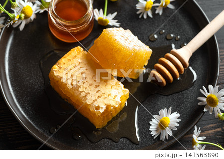 Golden honeycomb on white plate with chamomile flowers, fresh honey Golden honeycomb on white plate with chamomile flowers, fresh honey 141563890