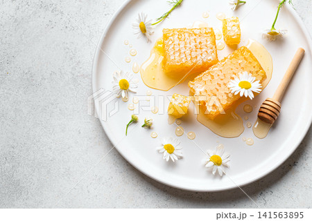 Golden honeycomb on white plate with chamomile flowers, fresh honey Golden honeycomb on white plate with chamomile flowers, fresh honey 141563895
