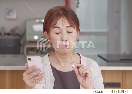 スマホと錠剤を手に健康管理をする女性 スマホと錠剤を手に健康管理をする女性 141563981