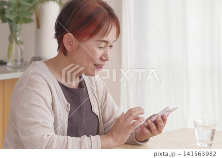 明るい室内でスマホを操作するシニア女性 141563982