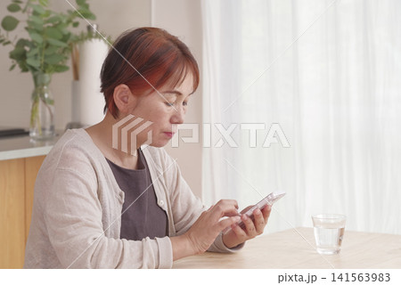 明るい室内でスマホを操作するシニア女性 明るい室内でスマホを操作するシニア女性 141563983