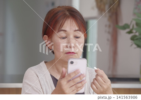 スマホと錠剤を手に健康管理をする女性 スマホと錠剤を手に健康管理をする女性 141563986