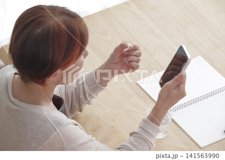 スマホと錠剤を手に健康管理をする女性 スマホと錠剤を手に健康管理をする女性 141563990