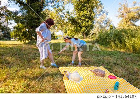 Young Caucasian girl and her mother using anti-mosquito spray in a sunny park enjoying nature while preventing insect bites during tick season. Wide shot 141564107