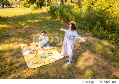 Yellow picnic blanket with mother and daughter resting in sunlight. Family communication and weekend getaway. Wide shot, top view Yellow picnic blanket with mother and daughter resting in sunlight. Family communication and weekend getaway. Wide shot, top view 141564108