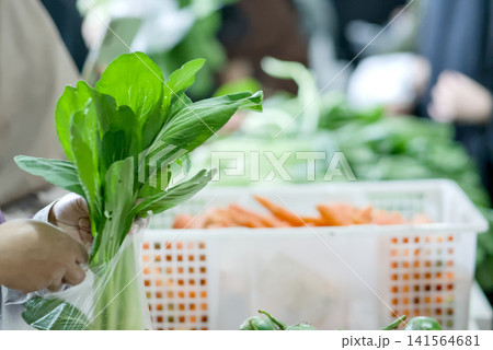 Closeup of hands selecting fresh green beans at a local farmers market, with blurred vegetable crates in the background, representing healthy eating and shopping	 141564681