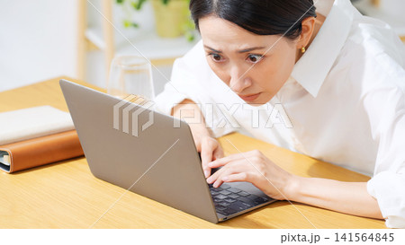 ノートPCにかじりついて見るミドル女性。真剣、仕事、投資、ギャンブル、熱中、集中、仕事、注目、不安 141564845