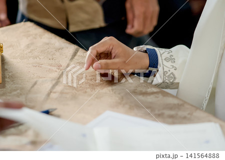 A close-up capture of a traditional wedding ceremony moment, highlighting the groom seated beside the officiant A close-up capture of a traditional wedding ceremony moment, highlighting the groom seated beside the officiant 141564888