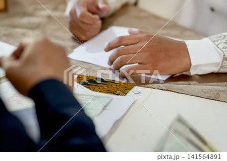 A close-up capture of a traditional wedding ceremony moment, highlighting the groom seated beside the officiant  141564891