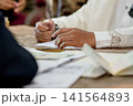 A close-up capture of a traditional wedding ceremony moment, highlighting the groom seated beside the officiant  141564893
