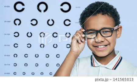 Smiling African American boy touching modern glasses frame during vision test. Pediatric ophthalmology diagnostic consultation and myopia correction. 141565813