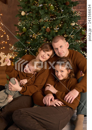 Family dressed in matching brown sweaters, gathered together in a warm, rustic room with a large Family dressed in matching brown sweaters, gathered together in a warm, rustic room with a large 141566634