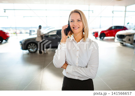 Businesswoman talking on smartphone at car dealership showroom Businesswoman talking on smartphone at car dealership showroom 141566657