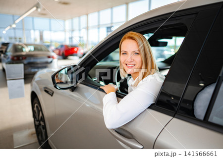 Woman smiling buying new car at dealership showroom Woman smiling buying new car at dealership showroom 141566661