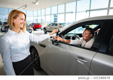 Saleswoman handing car keys to happy customer in showroom Saleswoman handing car keys to happy customer in showroom 141566676