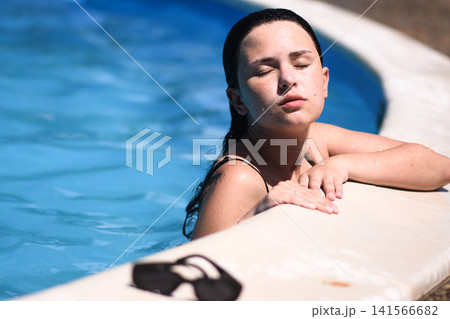 Woman relaxing in swimming pool with eyes closed creates summer wellness concept. Woman relaxing in swimming pool with eyes closed creates summer wellness concept. 141566682