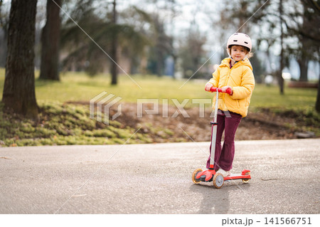 Young child riding scooter in park wearing helmet Young child riding scooter in park wearing helmet 141566751